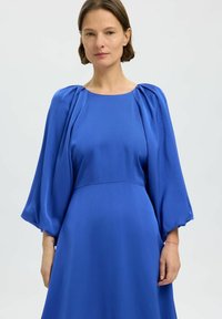 Vestido azul de tela suave, con mangas abullonadas y un escote redondo. La falda cae elegantemente hasta el suelo con un corsé ajustado.