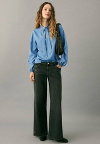 Camisa azul claro de manga larga con escote en forma de ojo de cerradura, combinada con jeans oscuros de pierna ancha con ligeros adornos. Complemento con bolso negro.