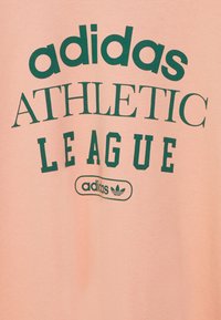 Šviesiai rožinė medvilninė marškinėliai su ryškiai žaliais užrašais "adidas ATHLETIC LEAGUE" ir maža klasikinė trijų dryžių logotipu.