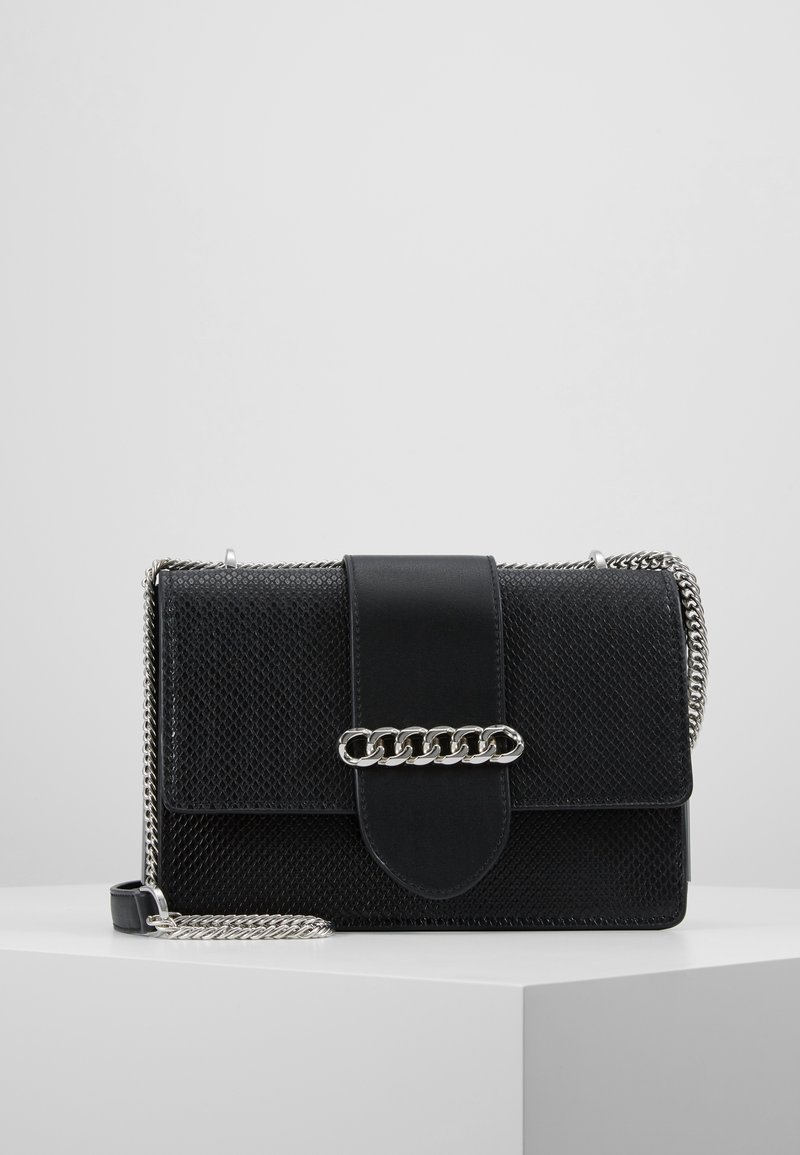Borsa nera in materiale texturizzato, con dettagli in metallo e chiusura a patta. Presenta una tracolla in metallo a catena removibile. Forma rettangolare.
