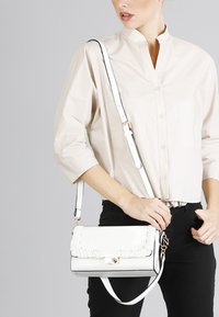 Hvid læder crossbody taske med plisserede detaljer, gyldent hardware og justerbar rem, der har en rektangulær form og lås.