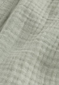 Lichtgroene gestructureerde stof met een rasterpatroon, met een geweven, linnenachtig uiterlijk. Zachte, gerimpelde textuur die de visuele diepte versterkt.