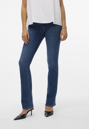 Mørkeblå denimjeans med slim fit, med en mid-rise livhøyde og subtile sømdetaljer. Kombinert med svarte spisse hæler.
