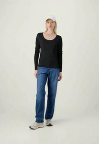 Μαύρη μπλούζα με μακριά μανίκια και στρογγυλή λαιμόκοψη, συνδυασμένη με μπλε τζιν ίσιας γραμμής και ανοιχτόχρωμα αθλητικά παπούτσια, φορεμένη με λευκό καπέλο.