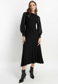 Czarna midi sukienka z długimi przezroczystymi wzorzystymi rękawami, dopasowaną górą i rozkloszowanym dołem. W zestawie ze szpilkami z długim czubkiem.