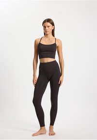 Brassière de sport noire à fines bretelles associée à un legging noir taille haute. Les deux sont près du corps avec une texture lisse et un minimum de coutures.