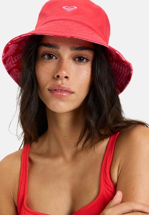 Roter Bucket Hat mit einer festen Außenlage und einem gemusterten Innenfutter. Mit einem kleinen Logo auf der Vorderseite und einer weichen Textur.