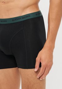 Boxeri negri cu un tiv elastic verde, având brandul "BJÖRN BORG"; material neted cu un design ajustat și o textură moale.