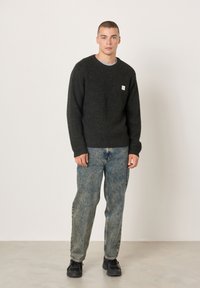 Tamnosivi rebrasti džemper s okruglim izrezom, upareni s izblijedjelim svijetloplavim trapericama i crnim tenisicama. Na džemperu se nalazi mali logo brenda.