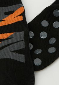 Černé ponožky s šedým a oranžovým grafickým designem a texturovanými silikonovými tečkami na podrážkách pro lepší trakci. Měkká pletená látka.