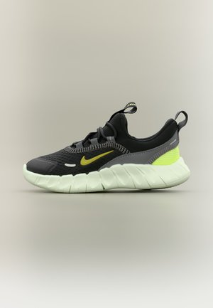 Fekete és szürke Nike sportcipő neon sárga részletekkel és vastag fehér talppal, oldalnézetből, semleges háttér előtt.