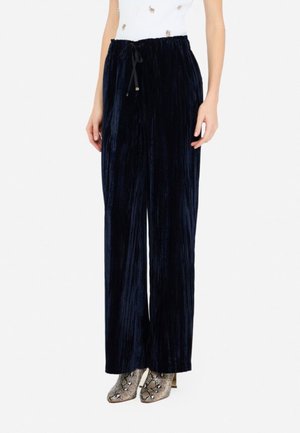 Pantaloni a palazzo in velluto blu navy con vita elastica e texture verticale a righe, abbinati a stivali alla caviglia con motivo.