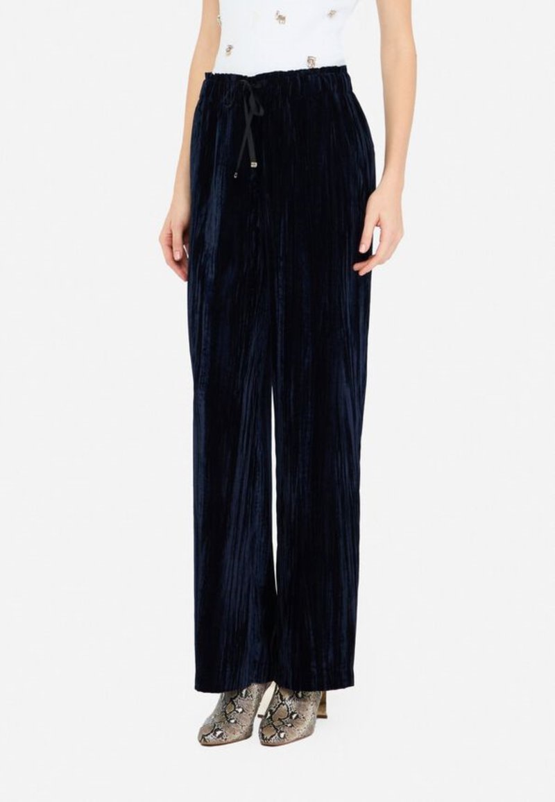 Pantaloni a palazzo in velluto blu navy con vita elastica e texture verticale a righe, abbinati a stivali alla caviglia con motivo.