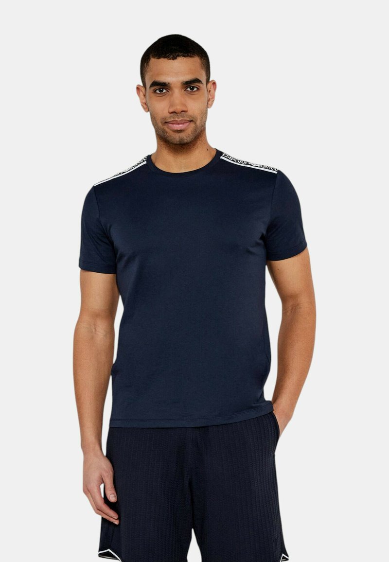 Marinblå t-shirt i slät tyg, med rund halsringning och korta ärmar med vita detaljer på axlarna.