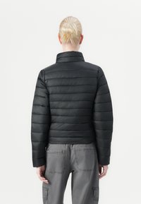 Svart polstret jakke med høy krage, med en quiltet design og en litt avkortet passform, kombinert med grå cargo-bukser.