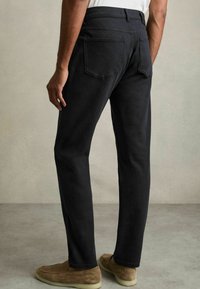 Pantaloni din denim închis, cu croială dreaptă și o textură netedă, prevăzuți cu buzunare la spate și o talie standard, asortați cu pantofi din suede de culoare maro deschis.