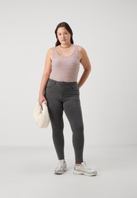 Top sin mangas a rayas con líneas naranjas, azules y blancas, combinado con unos jeans ajustados grises. Sosteniendo un bolso blanco, lleva zapatillas deportivas grises.