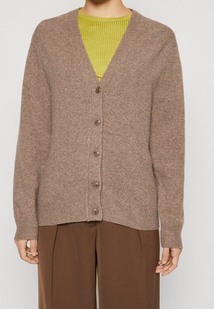 Personne portant un cardigan marron boutonné sur un haut côtelé vert citron et un pantalon marron à jambes larges, visible du cou aux hanches.