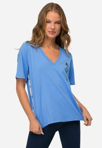 Lyseblå V-hals t-shirt med korte ærmer og en broderet blomstedesign på forsiden. Siderne har et kontrastmønster.