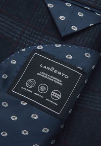 Granatowa tkanina z delikatnym wzorem w kratkę i białymi akcentami kwiatowymi. Zawiera etykietę z zaleceniami dotyczącymi pielęgnacji oraz cechy takie jak odporność na zagniecenia.