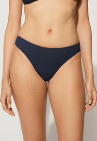 Tmavě modré bikiny s dnem vyrobené z texturované látky, s vysokým střihem a minimalistickým designem, mají hladký pás.