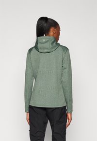 Zaļa struktūrēta kapuce ar pielāgotu kapuci un garām piedurknēm. Uzsvērta ģeometriska raksts un disks logotips kakla aizmugurē.