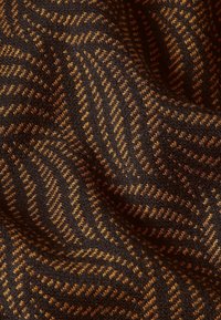 Textil med en strukturerad, fiskbensmönster i mörkbrunt och guld. Mjukt, vävt tyg som visar intrikata sömnadsdetaljer.