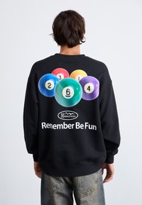 Black sweatshirt featuring a colorful billiard ball graphic and text "Remember Be Fun." Made of soft material, relaxed fit with ribbed cuffs.