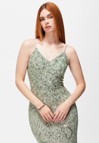 Abito da sera verde smeraldo con intricate perline e paillettes, vestibilità slim, scollatura a V e spalline sottili. Tessuto liscio e lucente.