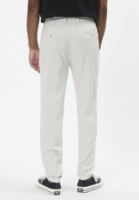 Hellgraue Hose aus strukturiertem Stoff, gerade geschnittene Beine, zwei Gesäßtaschen und schwarze Turnschuhe mit weißen Schnürsenkeln und Akzenten.