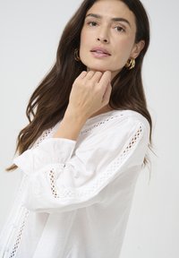 White blouse with lace accents on sleeves and a buttoned front, featuring a lightweight fabric and soft texture, styled with a relaxed fit.