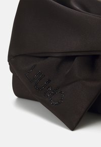 Tessuto di satin nero piegato con decorazioni di cristallo nero che formano la parola "LIU•JO" nell'angolo.