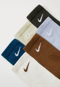 Five pairs of ribbed socks in various colors: dark green, light blue, brown, cream, and teal, each featuring a Nike logo in white.