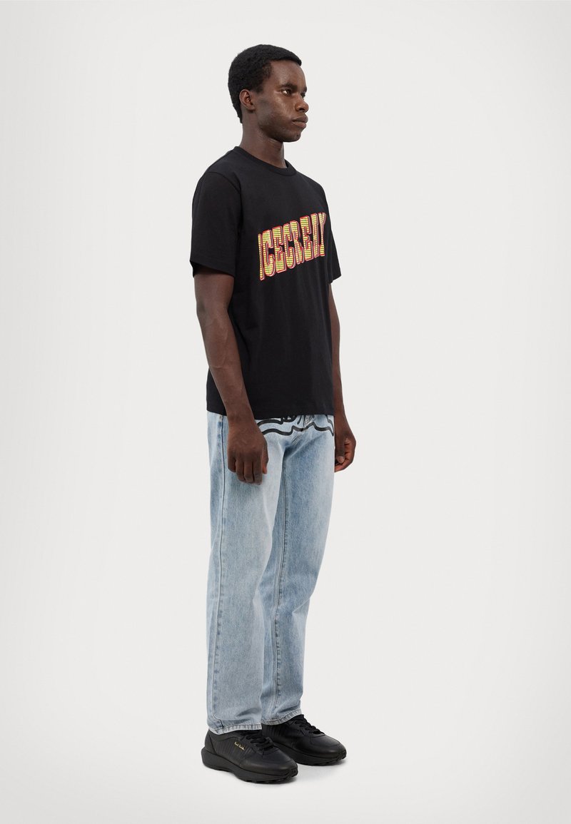 Black cotton T-shirt with "ACCESSIBILITY" in colorful text, paired with light blue denim jeans and black sneakers. Simple, casual design.