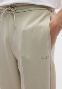 Beiget teksturoidut jogger-housut, joissa on joustava vyötärönauha ja nyöri. Varustettu sivutaskuilla ja hillityllä "BOSS"-logolla lahkeessa.