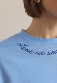Svetlo modra bombažna majica z okroglim izrezom in ukrivljenim vezenim napisom v temno modri barvi, ki se glasi "last at self."