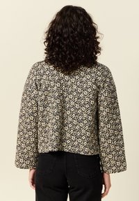 Czarna i kremowa kurtka w kwiatowy wzór, z długimi rękawami i luźnym krojem, z prostym dołem i teksturowanym materiałem.