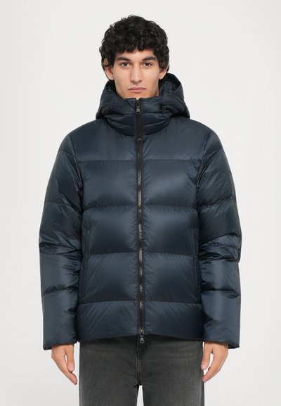 Chaqueta de plumas azul marino con diseño de acolchado horizontal, cierre de cremallera, capucha ajustable y textura suave y brillante. Modelo lleva pantalones grises.