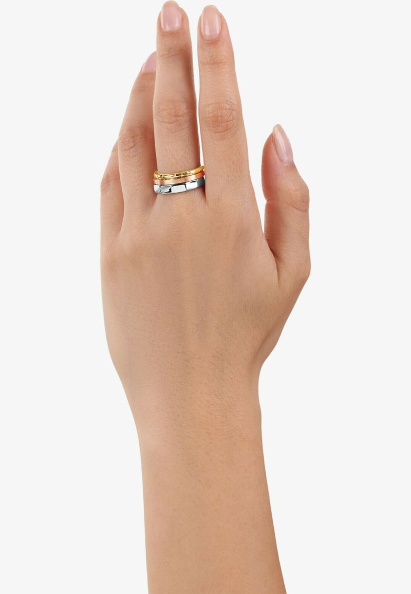 Tre anelli impilati su un dito: uno oro, uno argento e uno con una finitura lucida. Superfici lisce con bande di larghezze variabili.