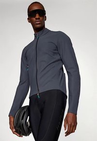 Veste de cyclisme ajustée pour homme en tissu extensible gris foncé avec une fermeture éclair, accompagnée d'un short de cyclisme noir et d'un casque.