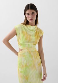 Cowl neck dress in yellow and green gradient with short sleeves, cut-out side, and smooth fabric featuring an abstract watercolor pattern.