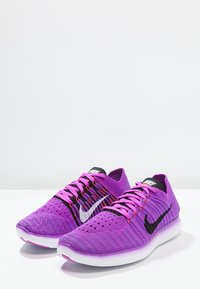 Zapatillas de correr moradas con un upper texturizado, swoosh de Nike en negro y blanco, punta afilada y una suela acolchada. Los cordones son de un morado claro.