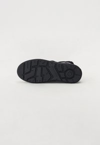 Suela de zapato de goma negra con un diseño texturizado que presenta surcos y patrones, proporcionando tracción y estabilidad.