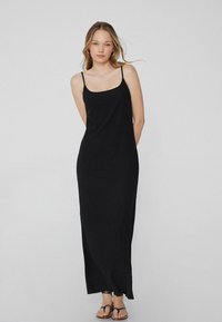 Schwarzes ärmelloses Maxikleid mit lockerer Passform, dünnen Trägern und einem bodenlangen Saum mit einem leicht ausgefransten Rand. Weicher Stoff.
