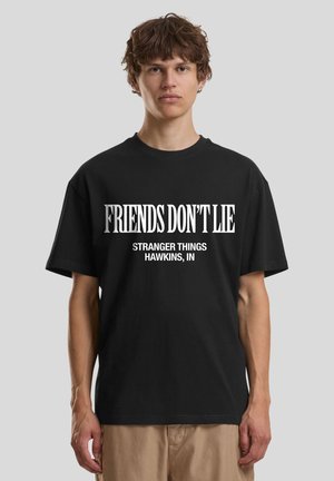 Čierne bavlnené tričko s krátkymi rukávmi s bielym nápisom: „PRIATEĽI NEKLAMÚ“ a „STRANGER THINGS HAWKINS, IN.“ Štandardný strih.