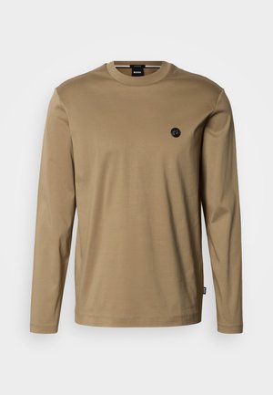 Tričko s dlouhým rukávem z lehké hnědé bavlny s kulatým výstřihem, s malou černou nášivkou loga na hrudi a s minimálními švy.