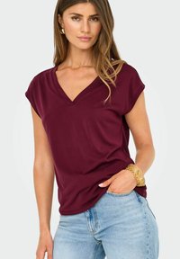 Blusa burdeos de cuello en V con mangas cortas, de tejido suave y corte relajado, combinada con vaqueros azul claro y una pulsera gruesa.
