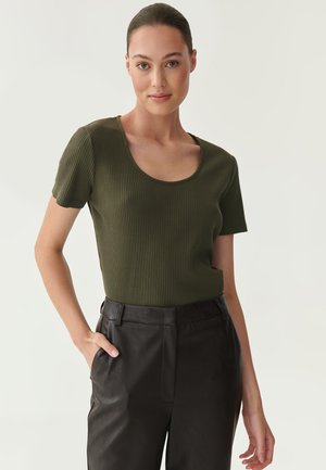 Olivgrünes, geripptes T-Shirt mit kurzen Ärmeln und rundem Ausschnitt. Kombiniert mit schwarzen Lederhosen mit seitlichen Taschen. Glatte Textur sichtbar.