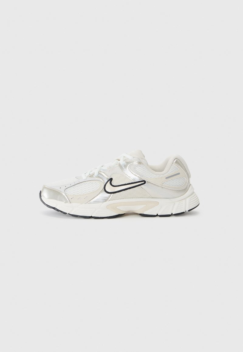 Bijela atletska cipela sa srebrnim naglascima, mrežastim panelima i crnim Nike swooshom. Teksturirana potplat za prianjanje i ublažavanje, sa vezicama.