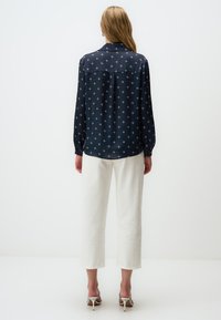 Marine blouse met een sterrenpatroon, lange mouwen en een kraag, gecombineerd met witte cropped broeken en lichte hakken. Gladde stoftextuur.